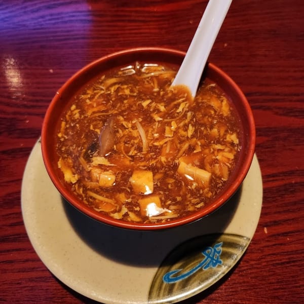 A red bowl of Ginbu 401's hot and sour soup with tofu, mushrooms, and egg, on a wooden table.