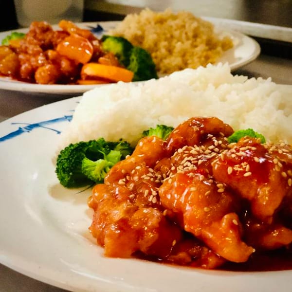 Two plates of Chinese orange chicken with white rice, broccoli, and sesame seeds.