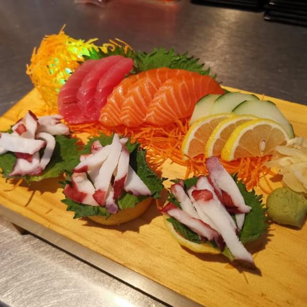 Sashimi platter with tuna, salmon, octopus, lemon, cucumber, and wasabi on a wooden board.